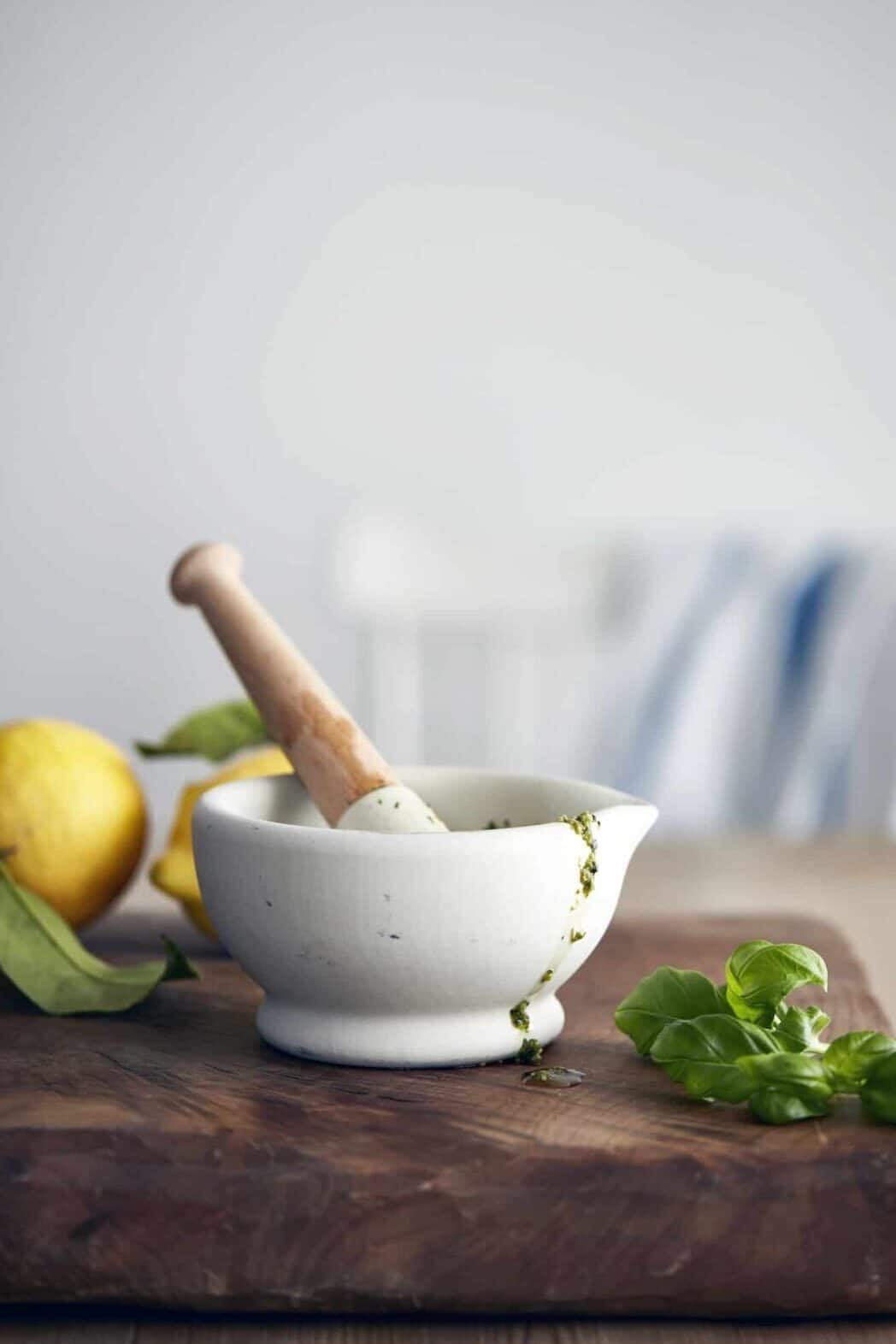 Pestle and mortar with pesto and basil on cutting board