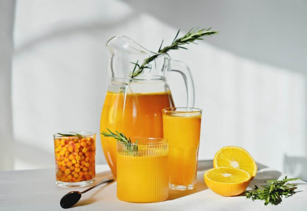 raw sea buckthorn and orange juice in glasses. with rosemary. antioxidant drink for immunity