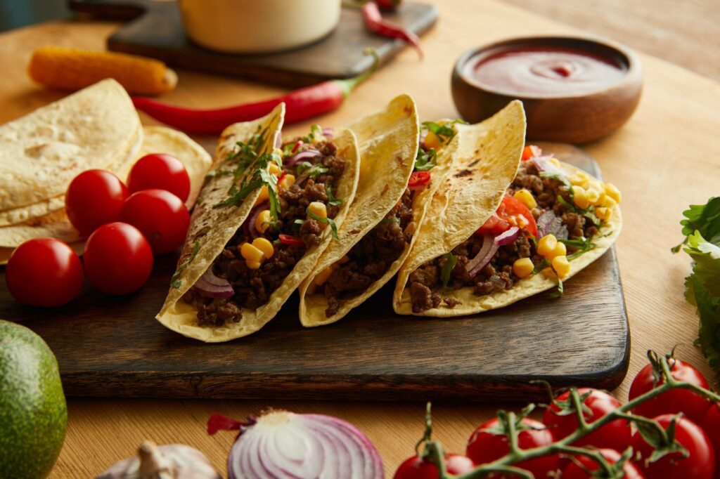 https://scratchmarket.co/wp-content/uploads/2022/12/fresh-tacos-with-minced-meat-and-vegetables-on-wooden-table-1024x682.jpg