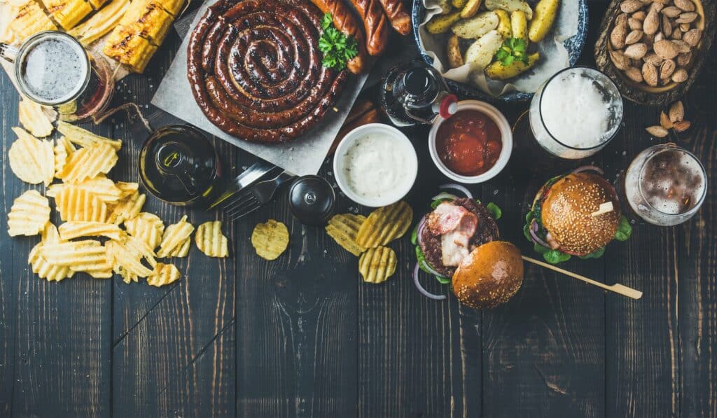 Variety of beers, sausages, burgers, potato, corn on dark background