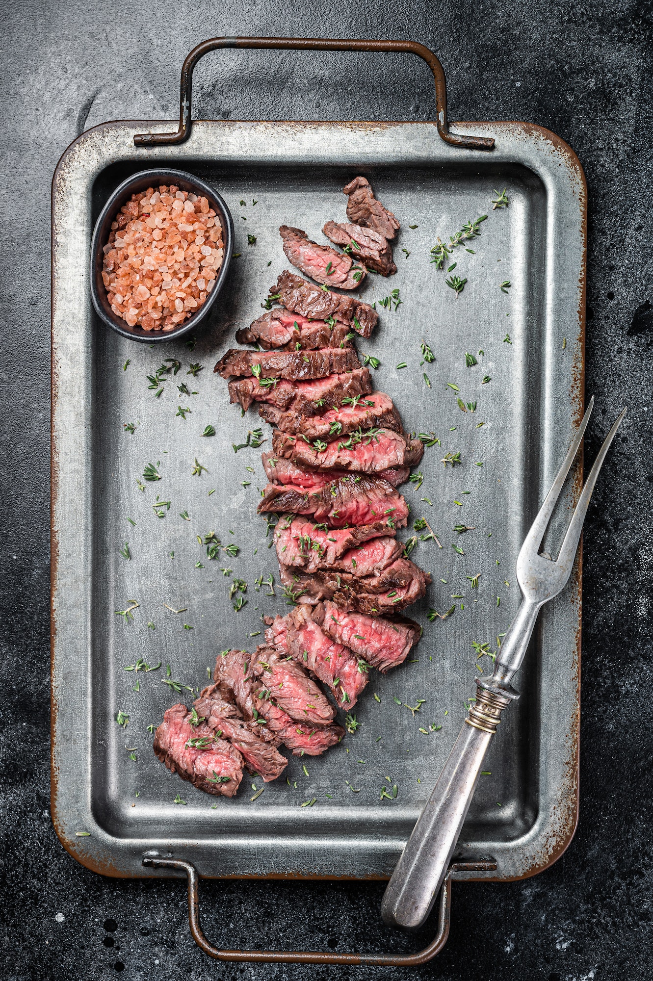 BBQ Roast sliced Skirt beef meat steak in steel tray with thyme. Black background. Top view
