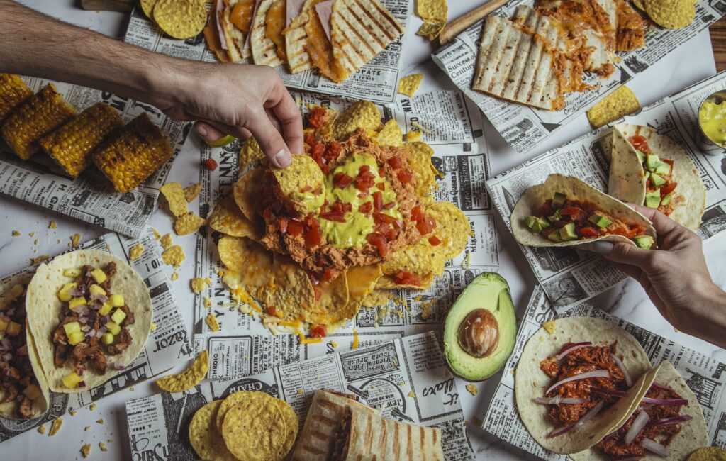 Friends dining on the Mexican taco. Shot of beef tacos, nachos and people hands, top view.