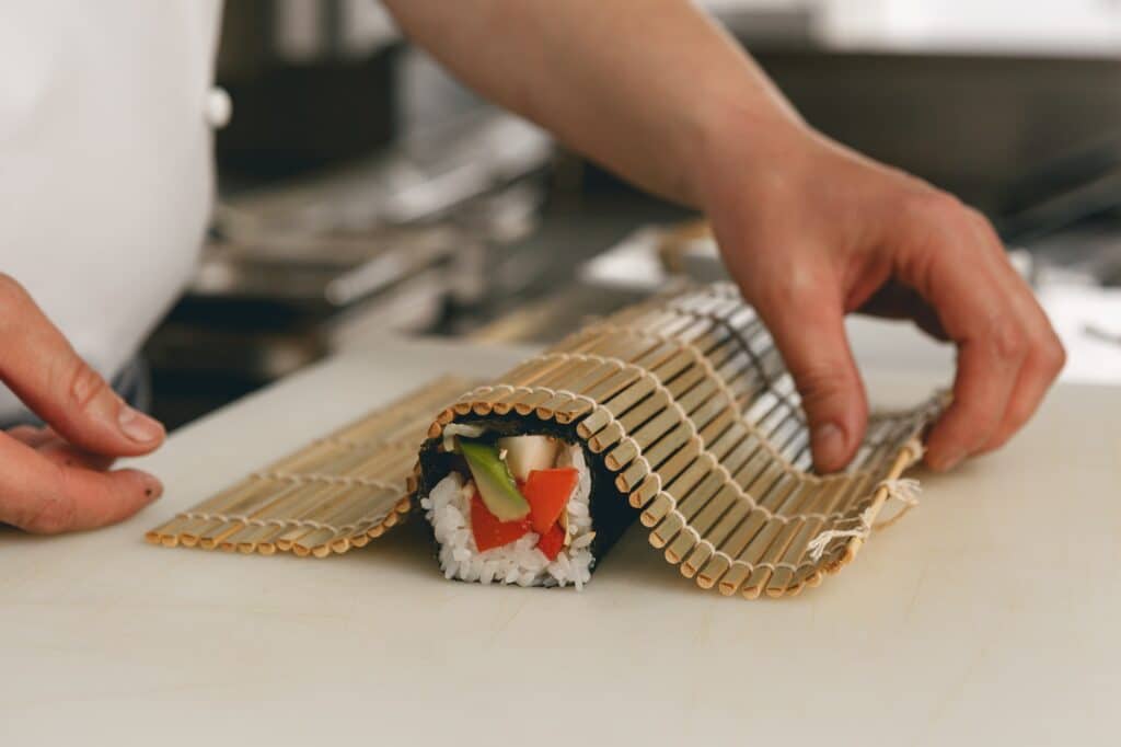Closeup of Chef hands rolling up sushi on bamboo mat in kitchen of restaurant